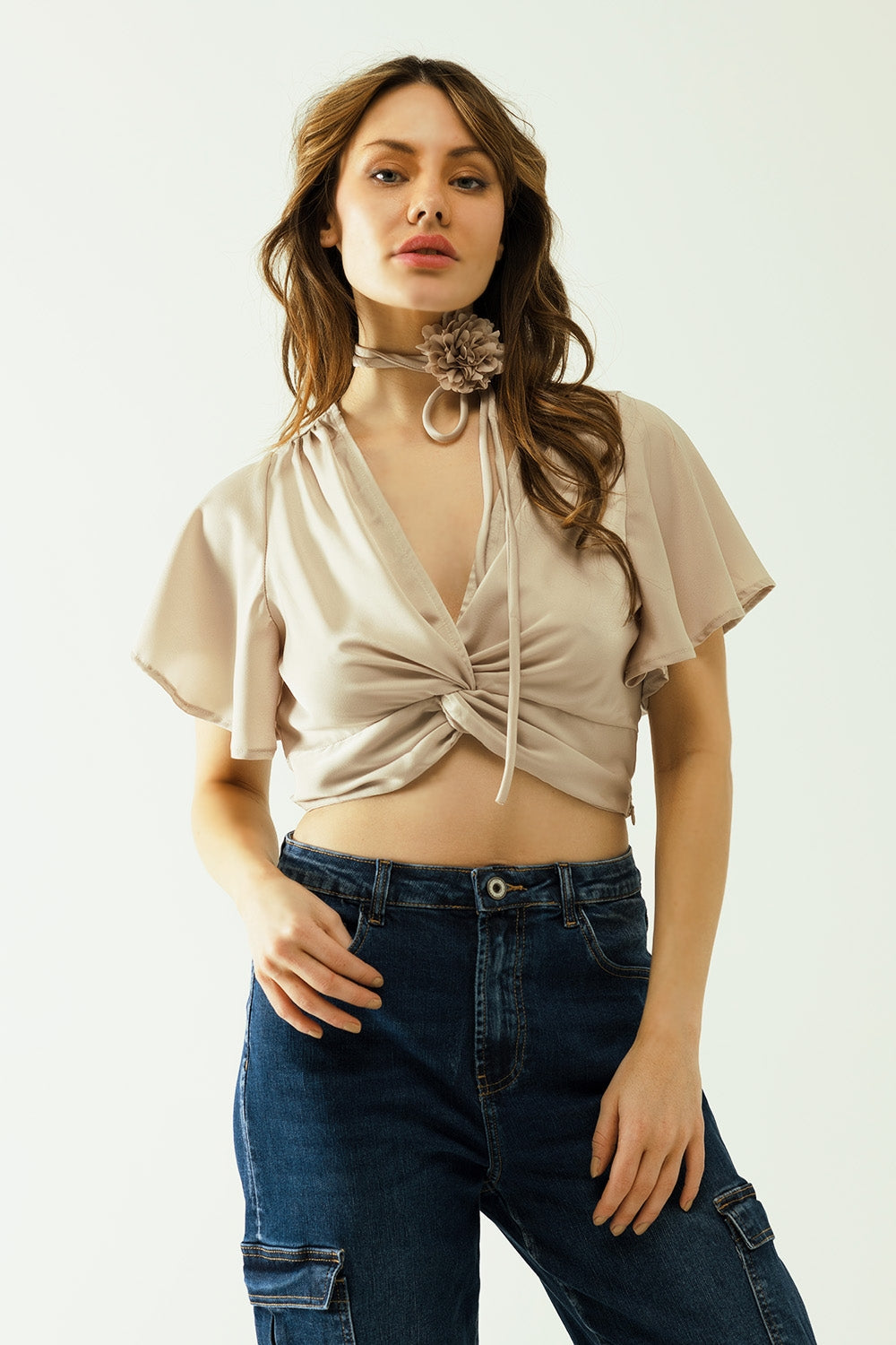 Beige V-neck crop top with short sleeves and a flower detail on the neck